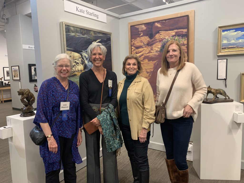 Four women standing in front of art at the Coors Western Art Exhibit and Sale: Linda Lillegraven, Kate Staring, Ann Korologos, and Sue Edmonds.